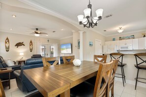 A dining area with a wooden table and chairs, a ceiling fan, and a kitchen in the background.