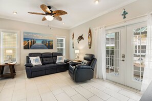 A living room with a black leather sofa, a recliner, a ceiling fan, and a large window with a view.