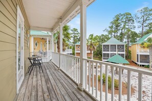 A wooden deck with a table and chairs, overlooking a landscaped area with buildings and trees.