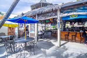Ein Außenbereich mit Bar, ausgestattet mit Tiki-Parasolen, Metallstühlen und einer Bar.