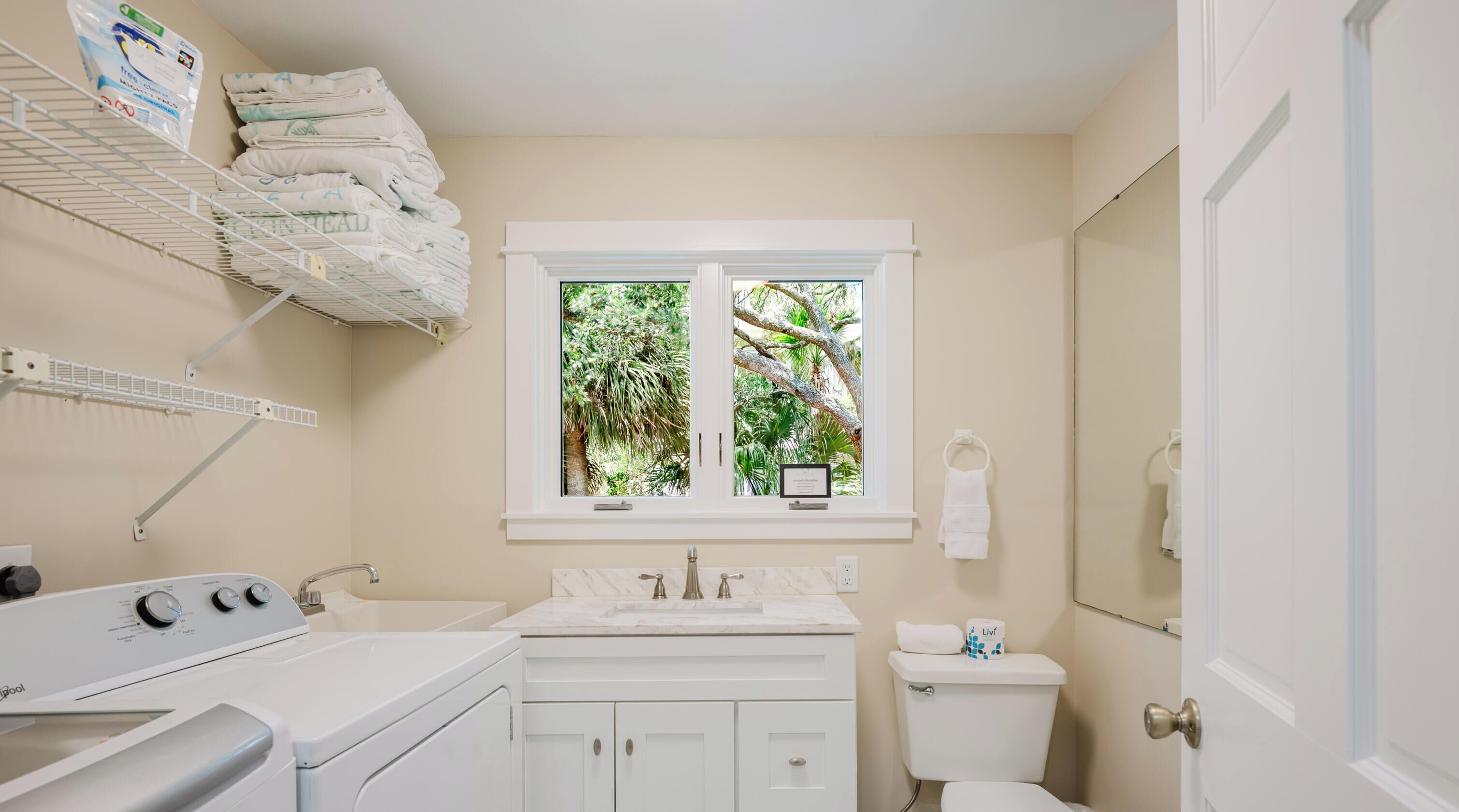 A bathroom with a window, a sink, a toilet, and a washing machine.