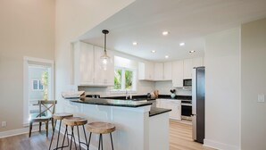 Una cocina moderna con armarios blancos, encimera negra y refrigerador de acero inoxidable.