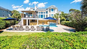 Una amplia casa de varios pisos con piscina, mobiliario exterior y exuberante jardinería.