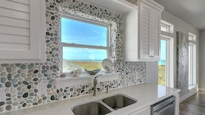 A kitchen with a stone backsplash, a window with a view, and white cabinetry.