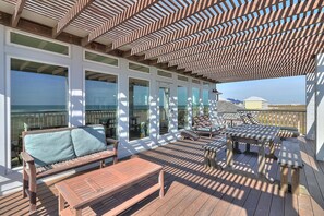 Eine überdachte Terrasse im Freien mit Holzmöbeln, großen Fenstern und Blick aufs Meer.