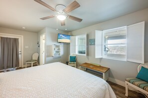 Ein Schlafzimmer mit einem Bett, einem Deckenventilator, einem Fernseher, einem Fenster mit Rollläden und Blick ins Freie.