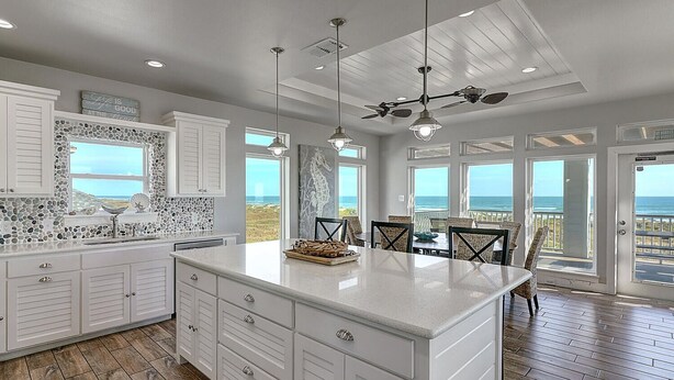 A spacious kitchen with a large island, white cabinetry, and a view of the ocean.