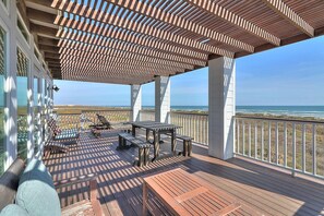 Eine überdachte Terrasse mit Blick auf das Meer, ausgestattet mit einem Tisch, Stühlen und einer Liege.
