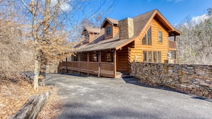 A log cabin with a stone wall, wooden deck, and a clear sky.