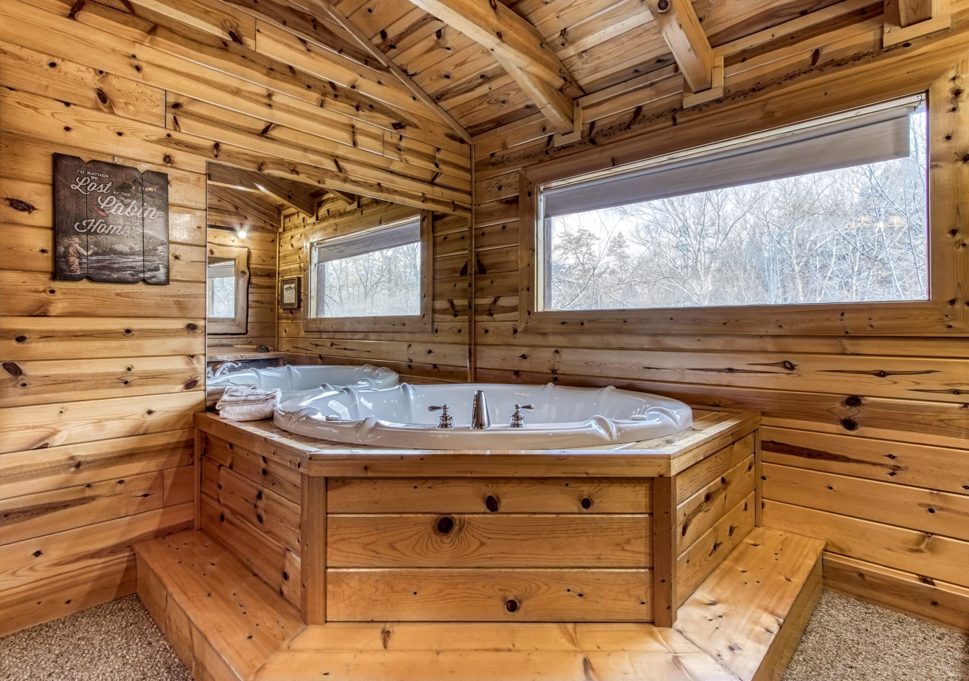 Interior de una cabaña de madera con una bañera de madera grande, paredes de madera y ventanas amplias.
