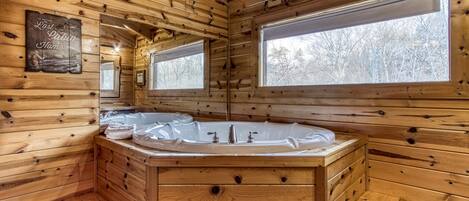 Interior de una cabaña de madera con una bañera de madera grande, paredes de madera y ventanas amplias.