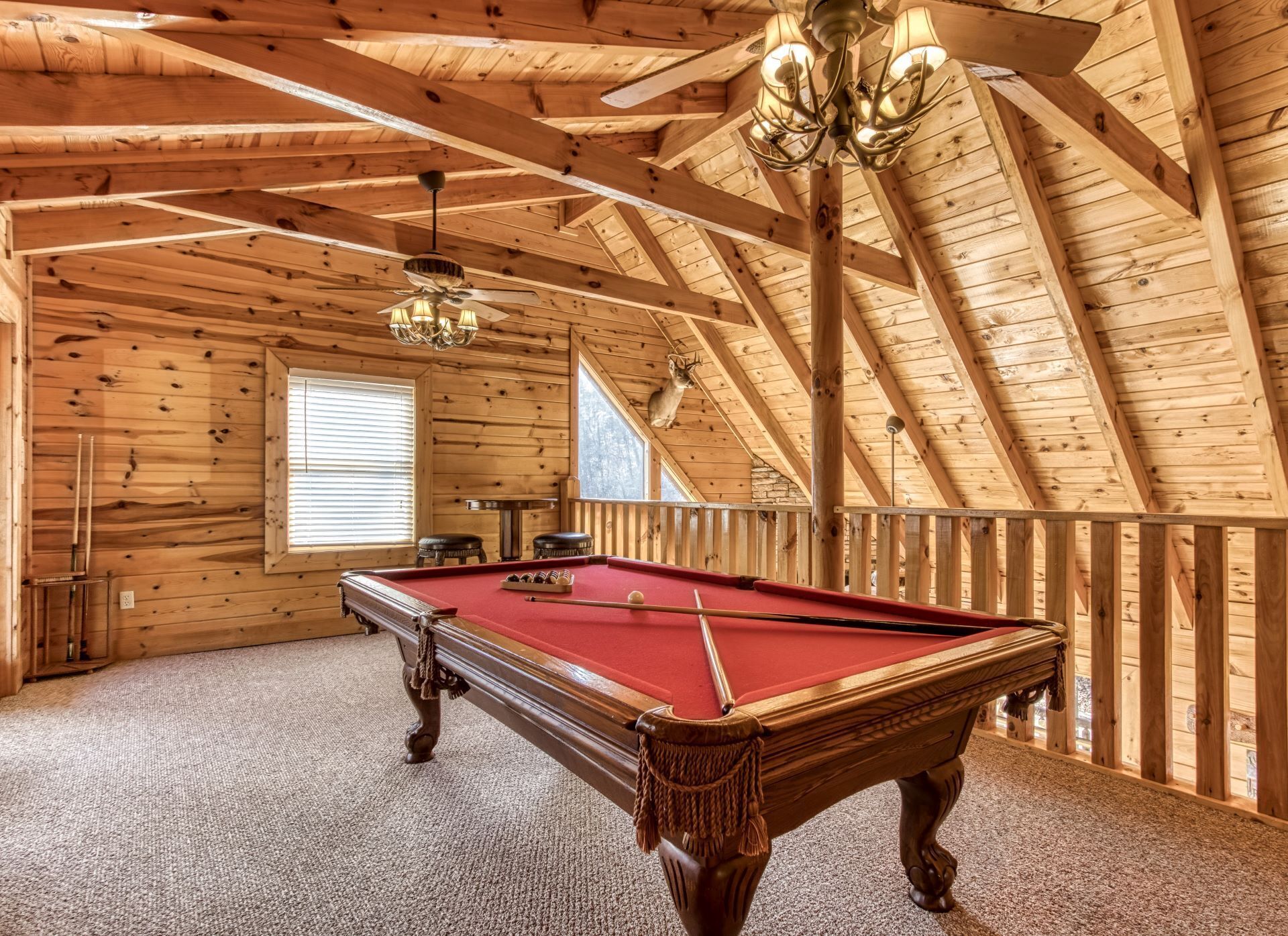 Un intérieur en bois avec une table de billard, un lustre et une fenêtre équipée de stores.