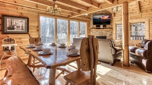 A wooden cabin interior with a dining table set for six, a leather sofa, and a stone fireplace.