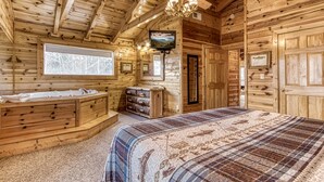 A log cabin bedroom with a large bed, a vanity with a sink, and a ceiling fan.