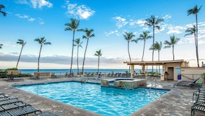 A pool area with lounge chairs and palm trees, overlooking the ocean.