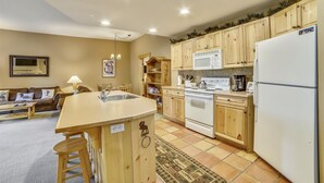 Una cocina con gabinetes de madera, un refrigerador blanco, una estufa y un microondas. Cuenta con un lavamanos y una zona de comedor con mesa y sillas.