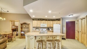 Una cocina compacta con armarios de madera, una isla central con taburetes, un microondas, una estufa y un refrigerador.