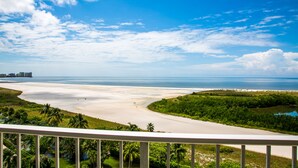 Rannikkomaisema, jossa on rantaa, vehreää kasvillisuutta ja kirkas taivas.
