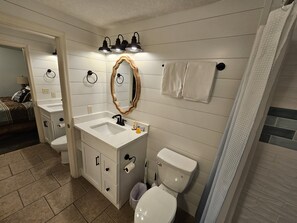 Un baño con tocador blanco, inodoro y espejo con marco de madera. Hay tres luces fijadas en la pared sobre el espejo.