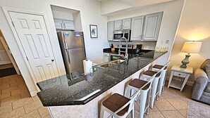 A kitchen with a central island, white cabinets, stainless steel appliances, and a bar stool seating arrangement.