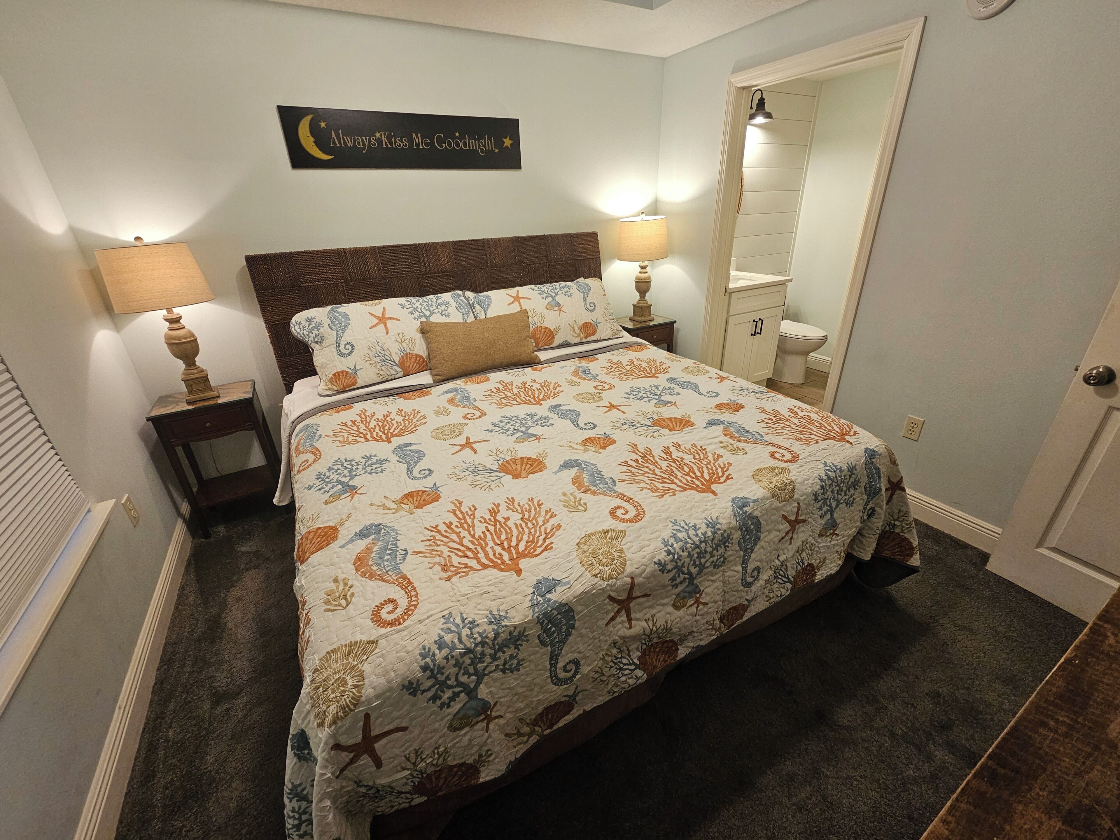 A bedroom with a bed, two bedside lamps, a nightstand, a mirror, and a wall sign.