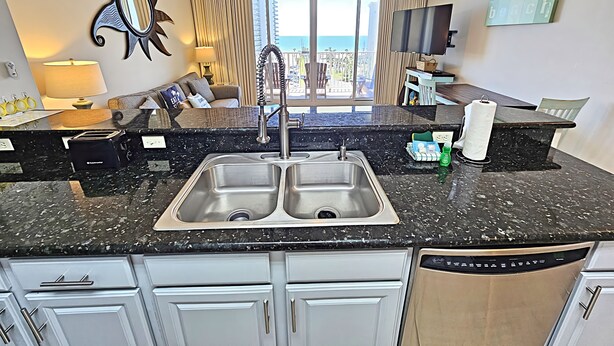 A modern kitchen with a double sink, granite countertop, and white cabinetry.