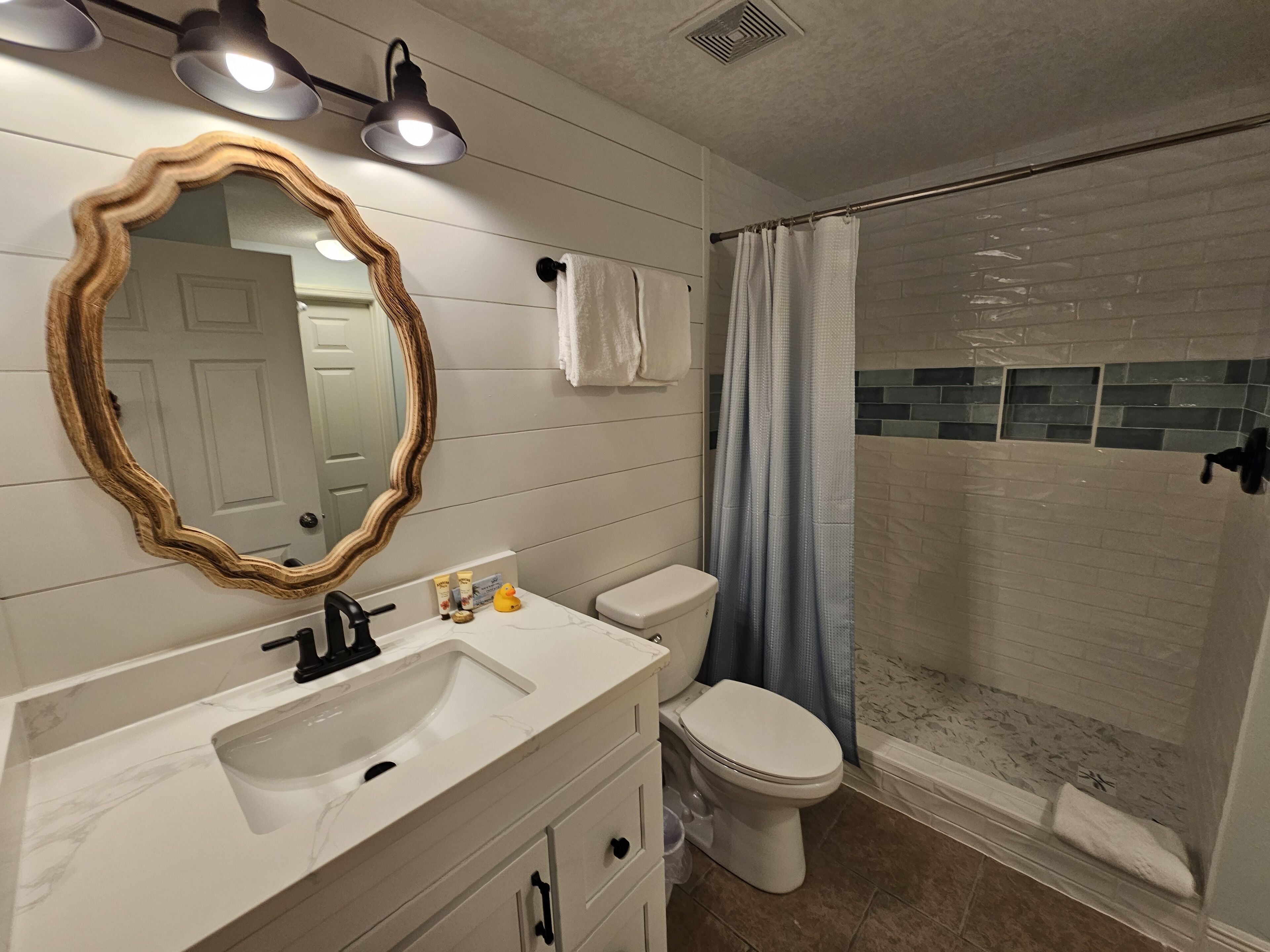 Une salle de bain avec un meuble-lavabo blanc, des toilettes, une douche avec une porte en verre et un miroir avec un cadre en bois.
