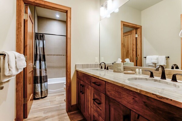 Un baño con tocador de madera, dos lavamanos, un espejo grande y una zona de ducha.