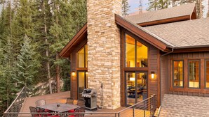 A modern log cabin with a stone chimney, large windows, and a deck with outdoor furniture. - Jane's Ski Chalet | Luxury Mountain Mansion | Sleeps 17 | Modern Decor | Private Hot Tub (Winter Park)