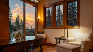 A cozy room with a large window, a wooden chair, a cushioned bench, and a small table with a lamp. - Jane's Ski Chalet | Luxury Mountain Mansion | Sleeps 17 | Modern Decor | Private Hot Tub (Winter Park)