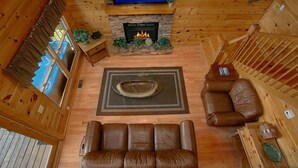 Interior acogedor de una cabaña con chimenea de piedra, sofá de cuero y televisor de pantalla plana sobre la chimenea.