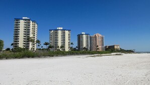 A beachfront hotel with multiple high-rise buildings, a sandy beach, and palm trees. - Escape To Beachfront Getaway Vacation Condo At Bargain Price! Heated Resort Pool! (Fort Myers Beach)