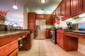 A kitchen with wooden cabinets, a stainless steel refrigerator, and a granite countertop. - 3BR Condo w  Resort Perks near Epic Universe! (Orlando)