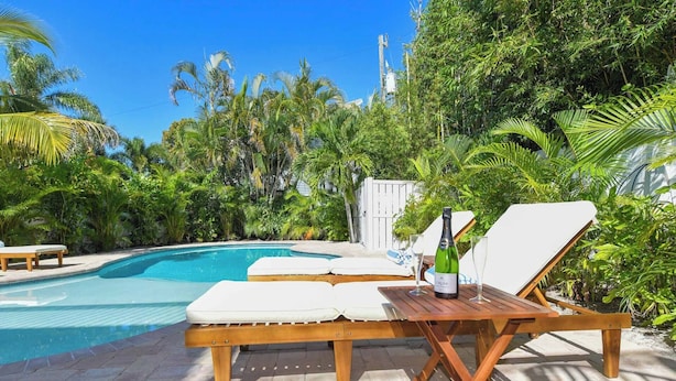 Un espace aménagé au bord de la piscine, avec des chaises longues, une table en bois et une bouteille de champagne.
