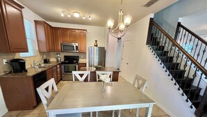Una cocina con armarios de madera, un refrigerador de acero inoxidable, un microondas y una mesa de comedor con sillas.