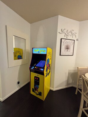 A Pac-Man arcade machine in a corner with a framed 'family' sign and a mirror on the wall.