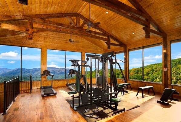 Ein Fitnessraum mit Trainingsgeräten und großen Fenstern mit Blick auf die Berge.