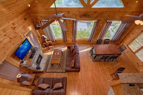 Uma cabana espaçosa com interior em madeira, um ventilador de teto, lareira, televisão e área de jantar.