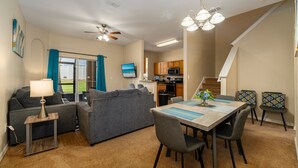A modern living room with a sofa, a dining table with chairs, a lamp, and a ceiling fan. - Town Home in Gated Resort with Lazy River & Waterslide Close to Attractions (Davenport)