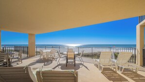 A covered outdoor area with lounge chairs, a table, and a view of the ocean.