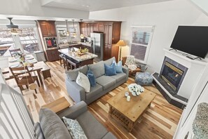 Et moderne køkken med en central ø, et spiseområde med et træbord, en stue med sofa og sofabord, samt en pejs.
