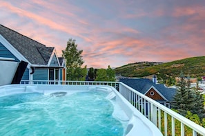 Un bain à remous sur un balcon offrant une vue sur un paysage vallonné et des maisons.