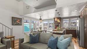 A spacious living room with a gray sofa, a dining area with a table and chairs, and a kitchen with dark cabinets and a refrigerator. - Abode on Woodside, private hot tub, walk to historic Main Street & trails (Park City)