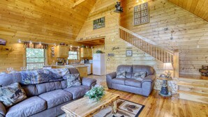 A spacious log cabin interior with a living room, kitchen, and a staircase.