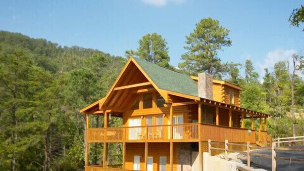 A wooden cabin with a balcony, set in a forested area.