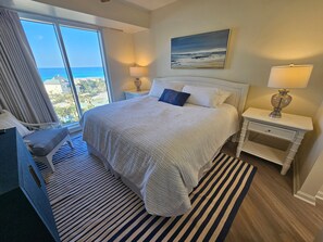 A hotel room with a large bed, a view of the ocean, a painting on the wall, and two bedside lamps. - Beachfront Condo Stunning 7th Floor Views and tram at Westwinds in Sandestin. Private beach (Miramar Beach)