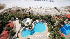 Vista aèria d'un complex turístic amb una gran piscina, parasols de platja i una zona de platja.