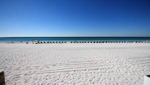 Platja ampla i sorrenca, amb cel blau clar i mar tranquil·la.