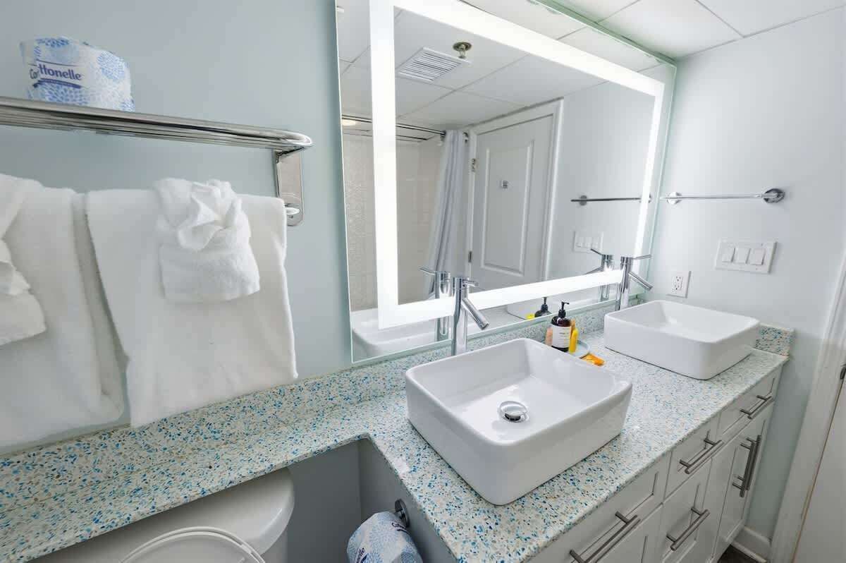 A modern bathroom with a large mirror, two sinks, and a glass shower enclosure.