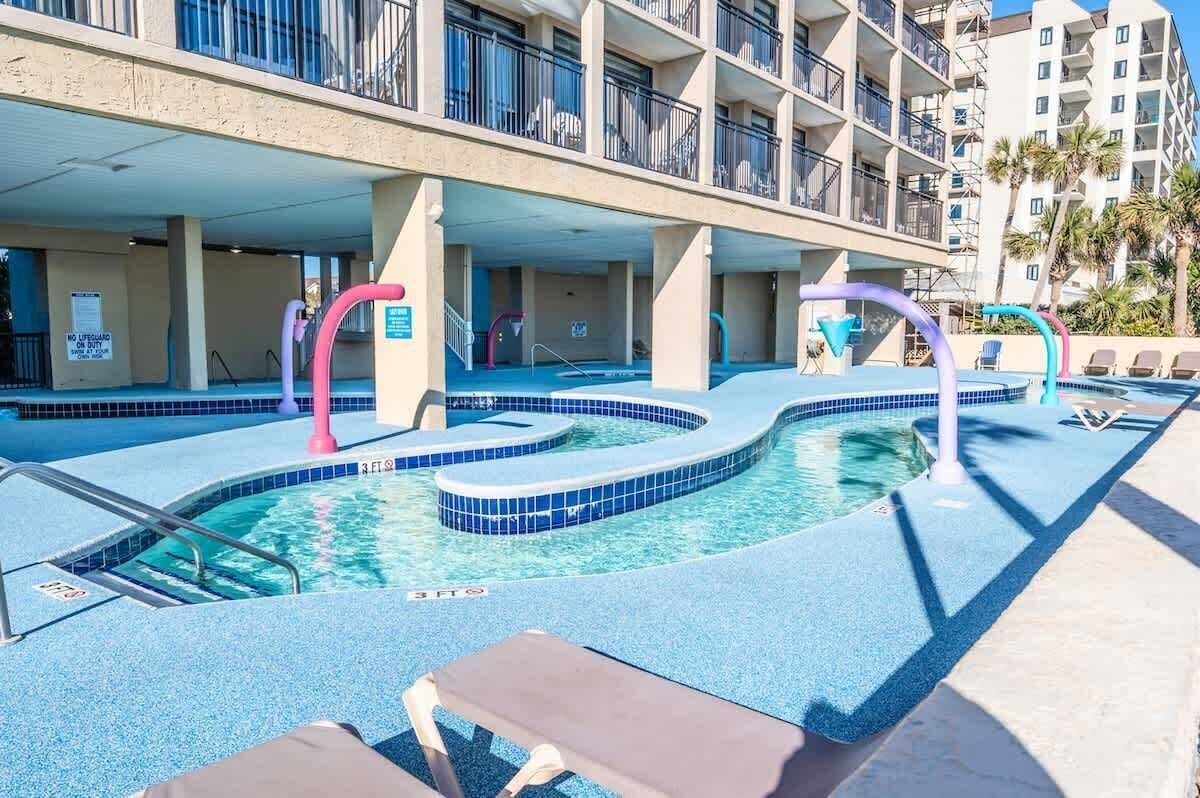 Une piscine au design original, entourée de chaises longues et d’un immeuble à plusieurs étages doté de balcons.